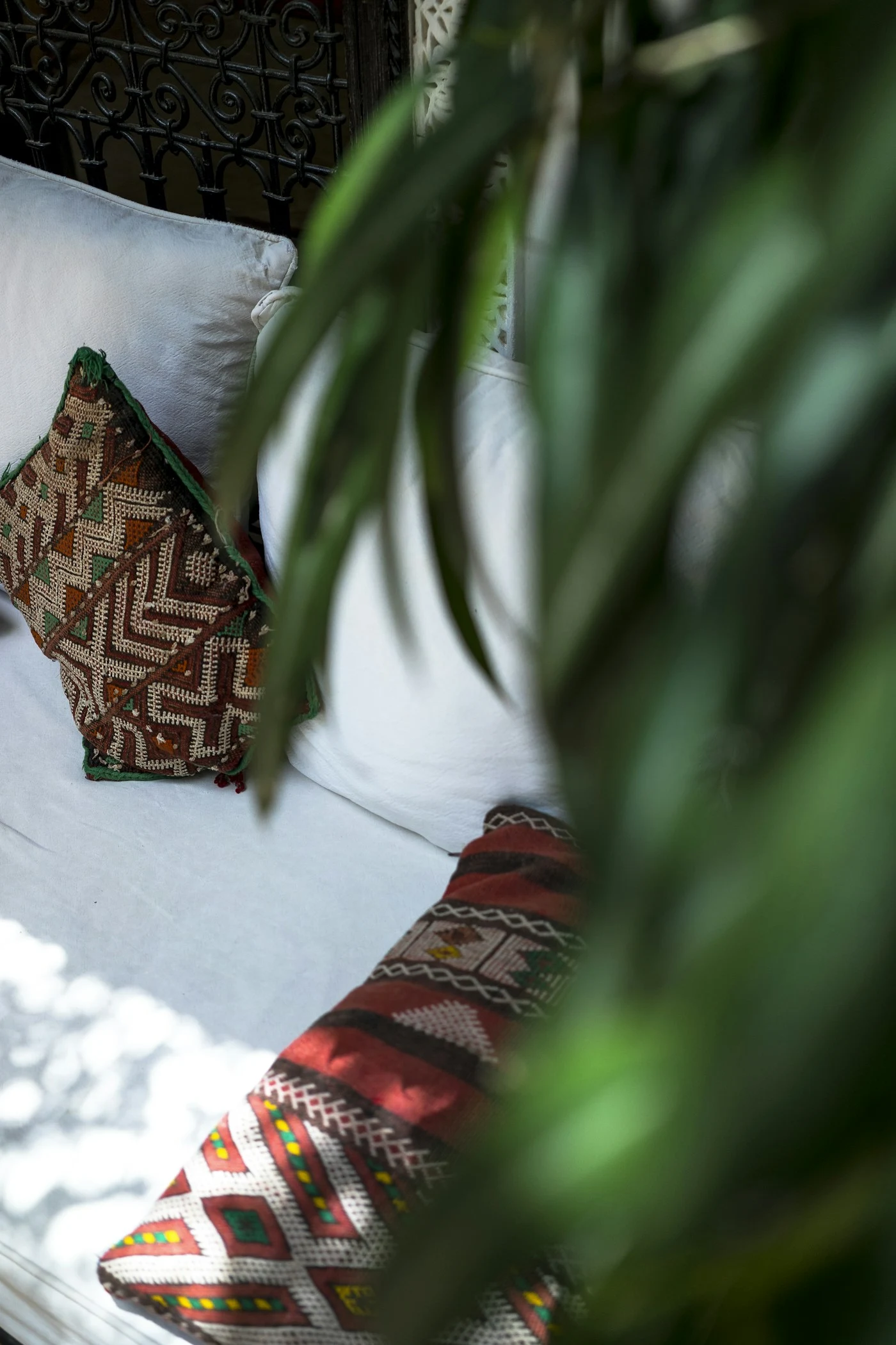 Coin détente d’un riad : banquette blanche, coussins marocains et feuillage